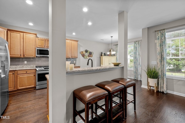 kitchen with an inviting chandelier, hanging light fixtures, decorative backsplash, light stone counters, and stainless steel appliances