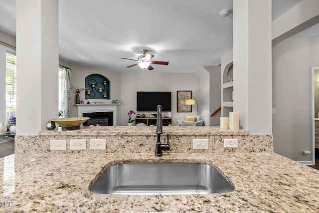 kitchen featuring ceiling fan, built in features, light stone countertops, and sink