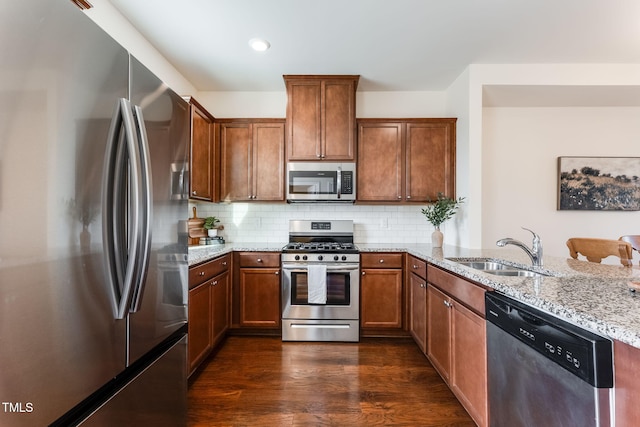 kitchen with stainless steel appliances, light stone countertops, sink, and dark wood-type flooring