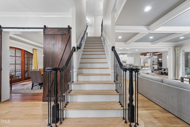 stairs with wood-type flooring, ornamental molding, a notable chandelier, beam ceiling, and a barn door