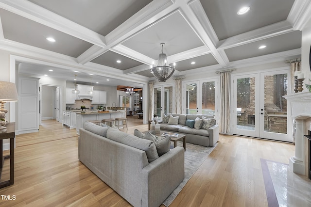 living room with a premium fireplace, french doors, a notable chandelier, light wood-type flooring, and coffered ceiling