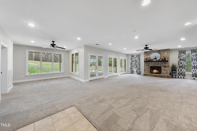 unfurnished living room featuring ceiling fan, light colored carpet, and a stone fireplace