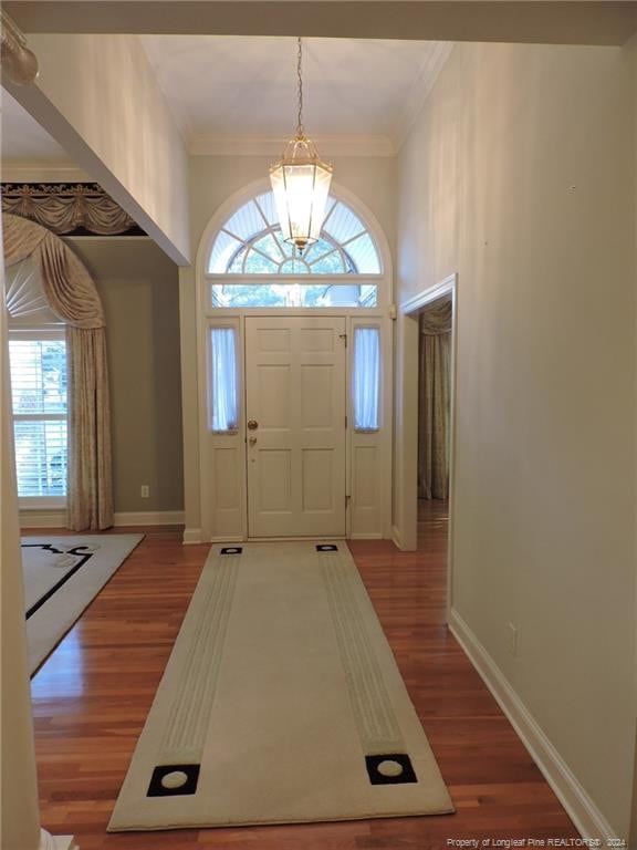 entryway with hardwood / wood-style floors, crown molding, and a notable chandelier