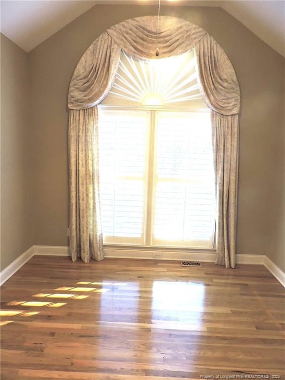 spare room with a wealth of natural light, dark hardwood / wood-style flooring, and vaulted ceiling