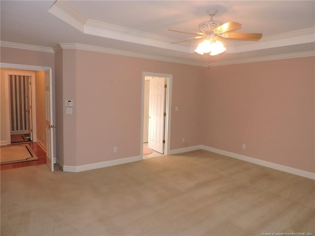 empty room featuring light colored carpet, a raised ceiling, ceiling fan, and ornamental molding