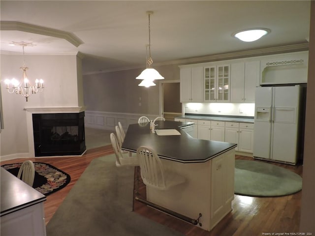 kitchen featuring white cabinets, a multi sided fireplace, hanging light fixtures, white fridge with ice dispenser, and ornamental molding