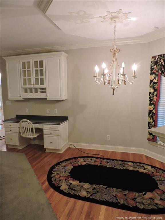 unfurnished dining area featuring hardwood / wood-style flooring, a notable chandelier, built in desk, and crown molding