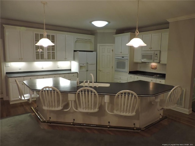 kitchen featuring a breakfast bar, sink, hanging light fixtures, white appliances, and a center island with sink