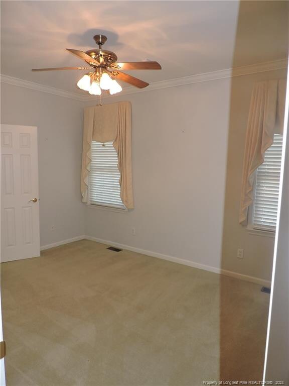 carpeted empty room featuring ceiling fan and crown molding