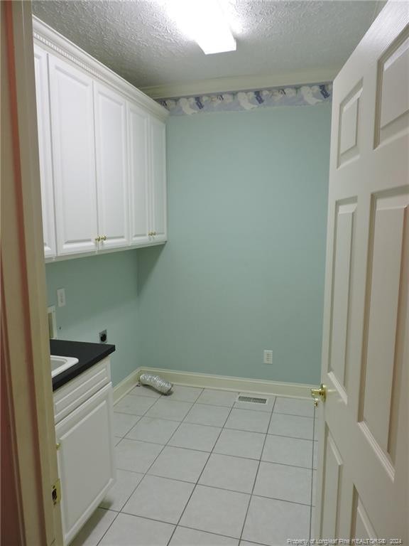 clothes washing area featuring cabinets, a textured ceiling, electric dryer hookup, and light tile patterned flooring