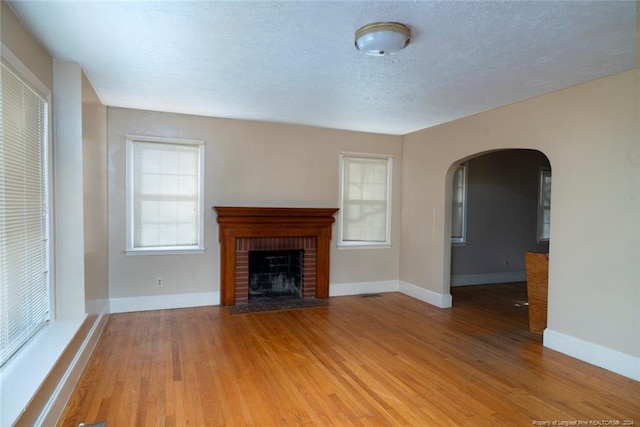 unfurnished living room featuring hardwood / wood-style flooring, a textured ceiling, and a brick fireplace