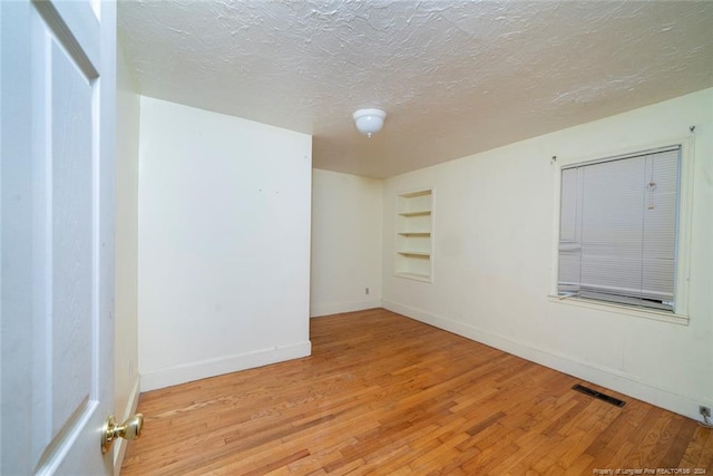 spare room featuring built in features, light hardwood / wood-style floors, and a textured ceiling