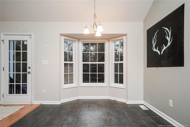 unfurnished dining area featuring plenty of natural light, a chandelier, and dark tile patterned floors