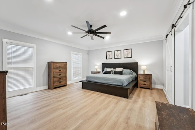 bedroom with a barn door, ceiling fan, crown molding, and light wood-type flooring