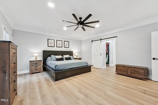 bedroom with ceiling fan, a barn door, light wood-type flooring, a spacious closet, and a closet