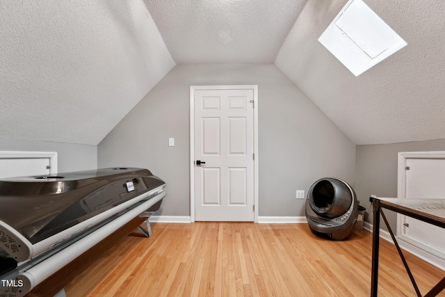 interior space featuring vaulted ceiling with skylight, a textured ceiling, and light hardwood / wood-style flooring