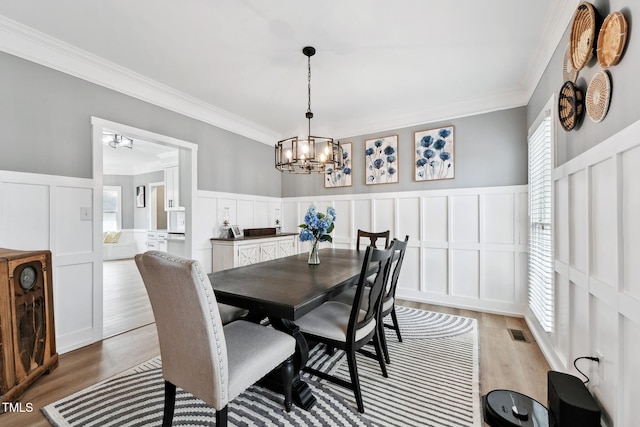 dining space with light hardwood / wood-style floors, ornamental molding, and a notable chandelier