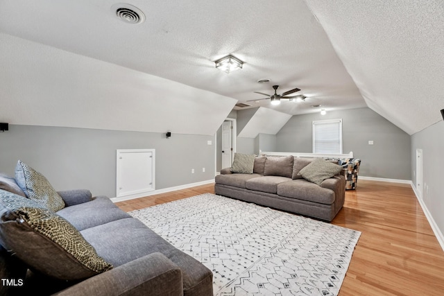 living room with a textured ceiling, ceiling fan, hardwood / wood-style floors, and vaulted ceiling