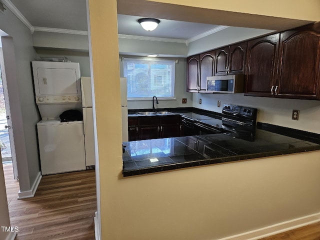 kitchen with stacked washing maching and dryer, ornamental molding, dark brown cabinetry, sink, and black electric range oven