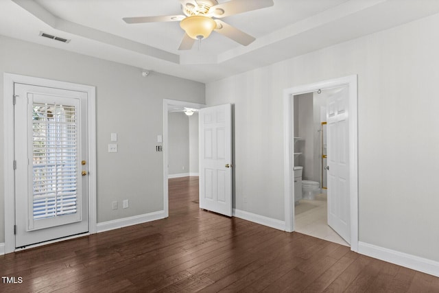 unfurnished bedroom with wood-type flooring, connected bathroom, a tray ceiling, and ceiling fan