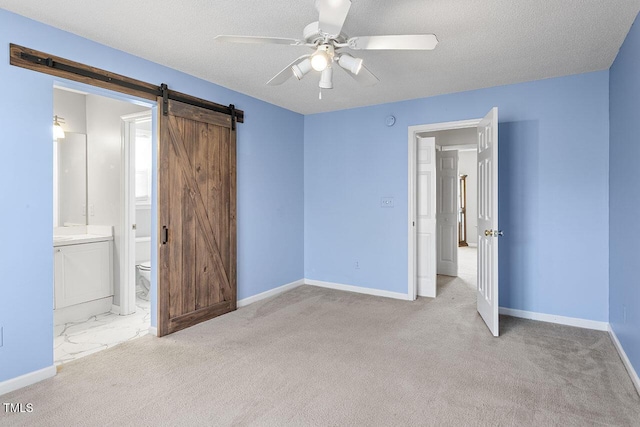 unfurnished bedroom with ceiling fan, a barn door, ensuite bathroom, and light carpet