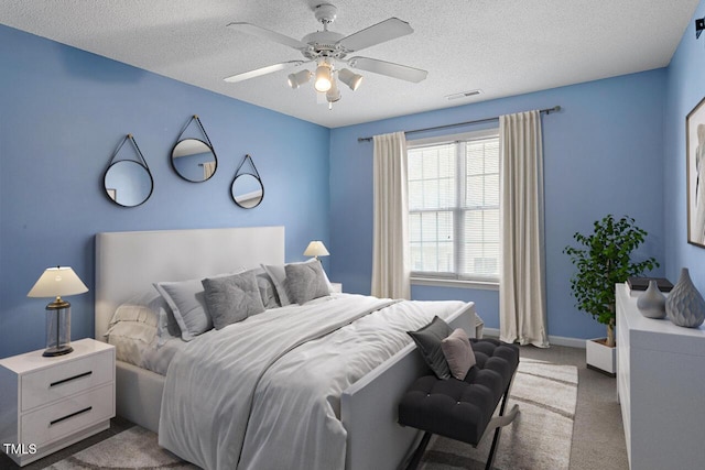 bedroom with ceiling fan, light colored carpet, and a textured ceiling