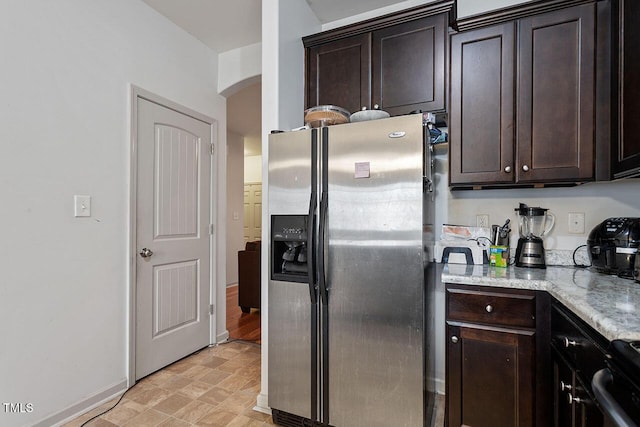 kitchen featuring stainless steel fridge, dark brown cabinets, and light stone countertops