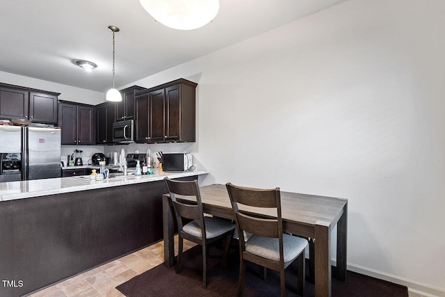 kitchen featuring pendant lighting, sink, light stone countertops, dark brown cabinets, and stainless steel appliances