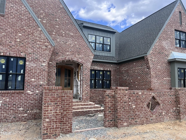 view of exterior entry featuring brick siding, roof with shingles, and board and batten siding