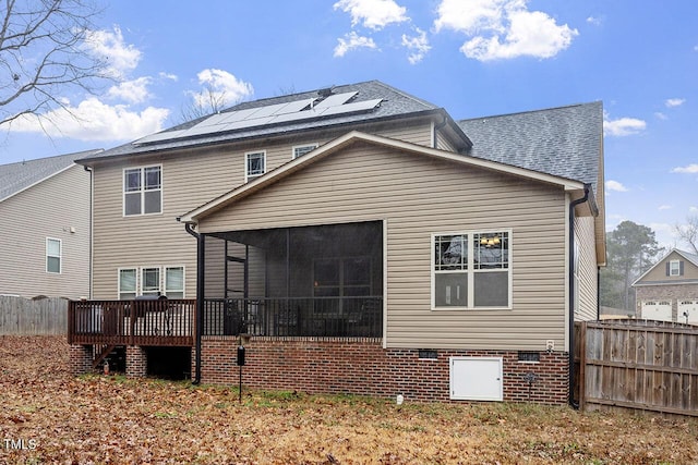 back of property featuring a sunroom, a deck, and solar panels