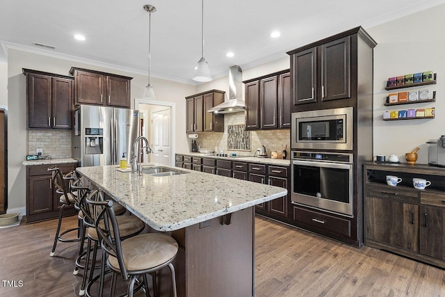 kitchen featuring decorative backsplash, appliances with stainless steel finishes, sink, wall chimney range hood, and a center island with sink