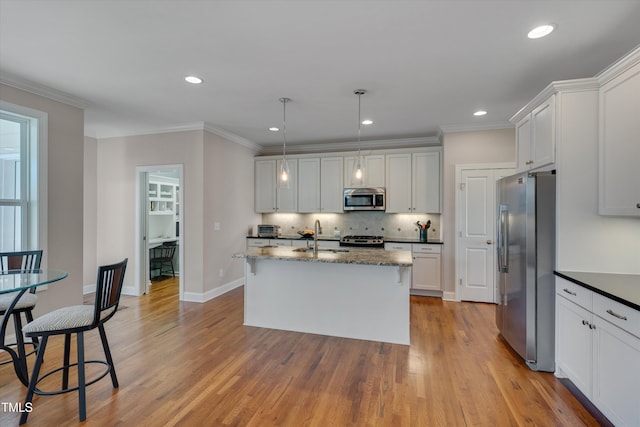 kitchen with pendant lighting, stainless steel appliances, a center island with sink, white cabinets, and sink