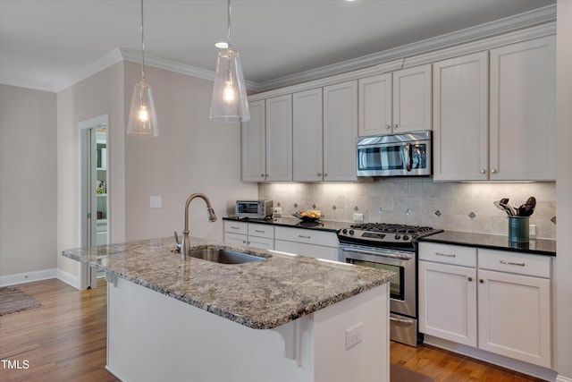 kitchen featuring hanging light fixtures, stainless steel appliances, a kitchen island with sink, dark stone countertops, and sink