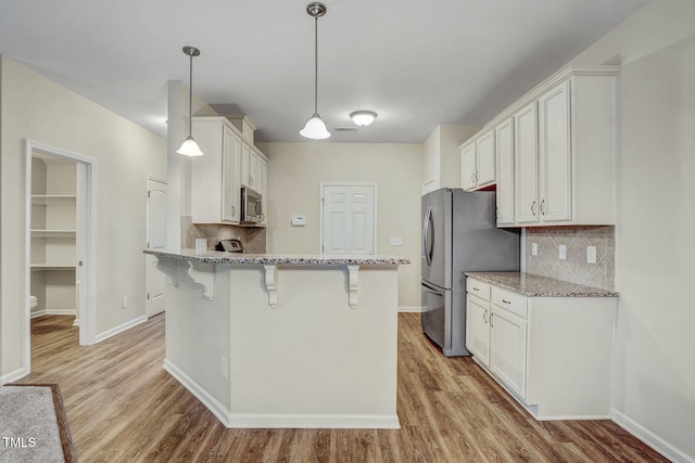 kitchen with white cabinets, appliances with stainless steel finishes, decorative backsplash, and pendant lighting