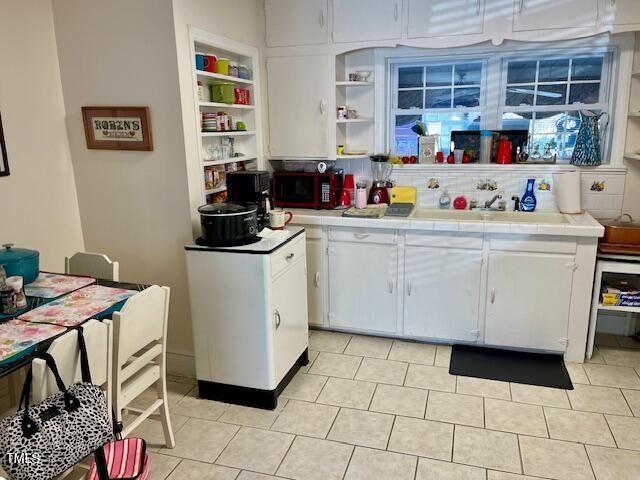 kitchen featuring tile countertops, white cabinets, sink, built in shelves, and light tile patterned floors