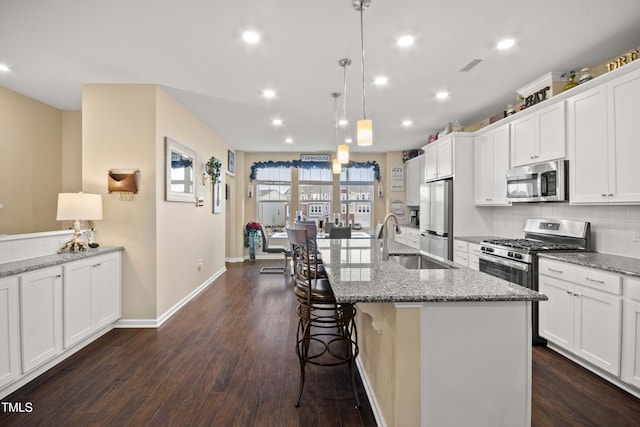 kitchen featuring stainless steel appliances, sink, pendant lighting, white cabinets, and an island with sink