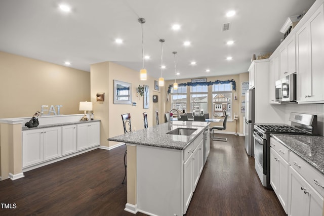 kitchen featuring visible vents, a center island with sink, stainless steel appliances, white cabinetry, and a sink