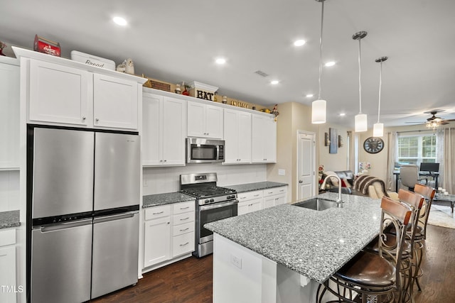 kitchen with a breakfast bar, stainless steel appliances, dark wood-style floors, white cabinetry, and a sink