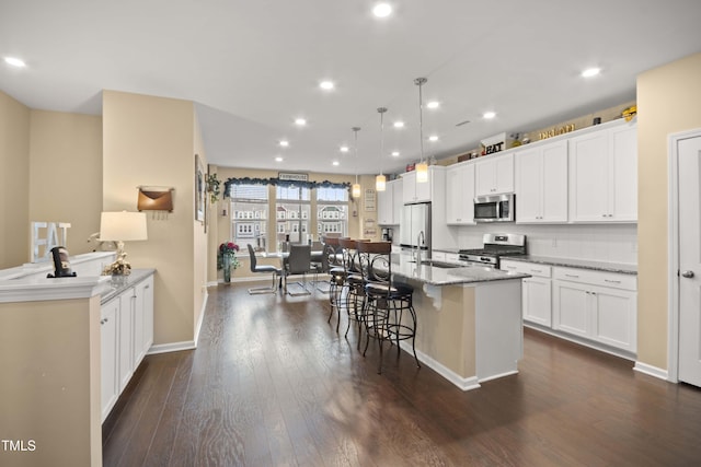 kitchen with a center island with sink, a sink, stainless steel appliances, dark wood-type flooring, and a kitchen bar