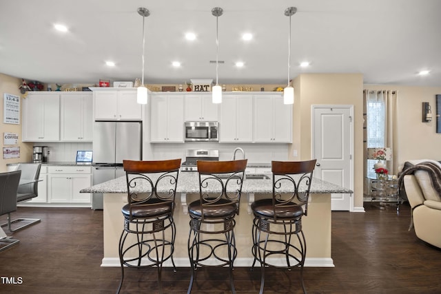 kitchen with light stone countertops, stainless steel appliances, a kitchen island with sink, hanging light fixtures, and a breakfast bar area