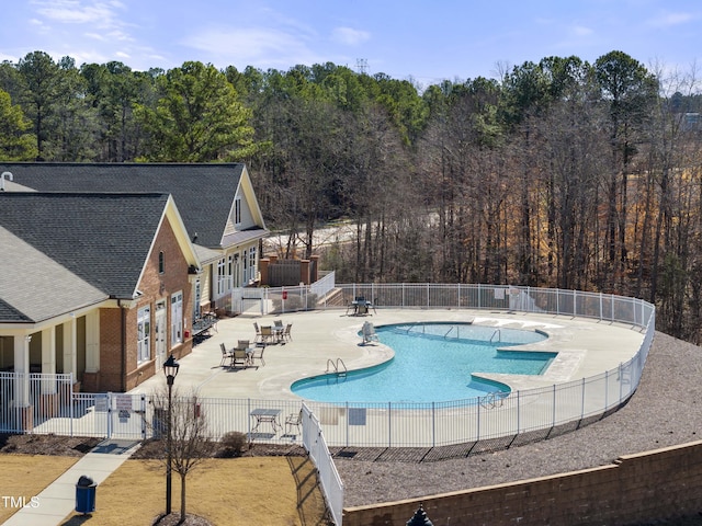 community pool featuring a patio area, a view of trees, and fence