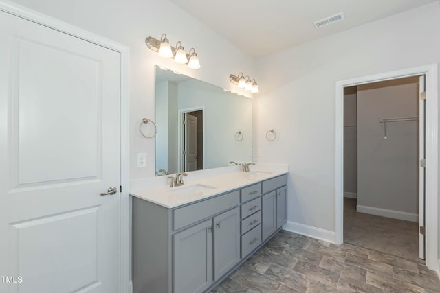 bathroom featuring visible vents, a walk in closet, a sink, double vanity, and baseboards