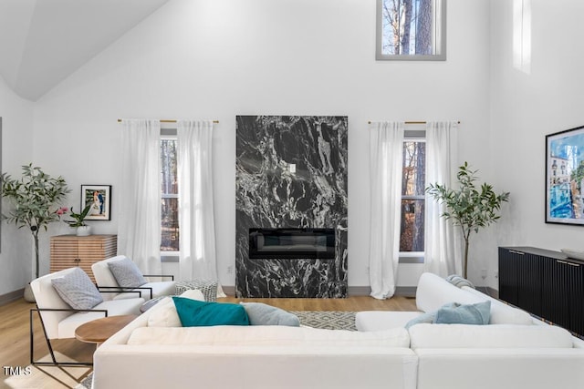 living room featuring high vaulted ceiling, radiator heating unit, a high end fireplace, and light wood-type flooring