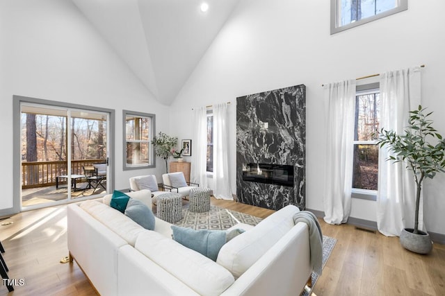 living room with light wood-type flooring, a high end fireplace, and a towering ceiling