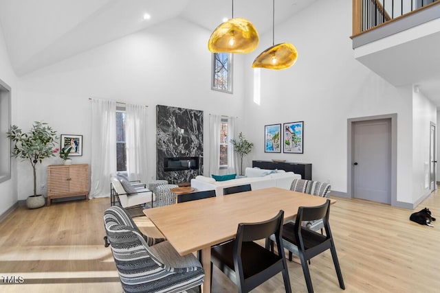 dining space with light wood-type flooring, a premium fireplace, and a high ceiling