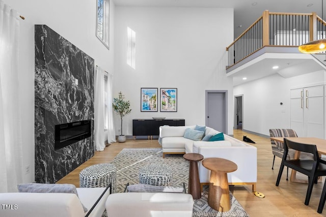 living room featuring light hardwood / wood-style floors, a premium fireplace, and a towering ceiling