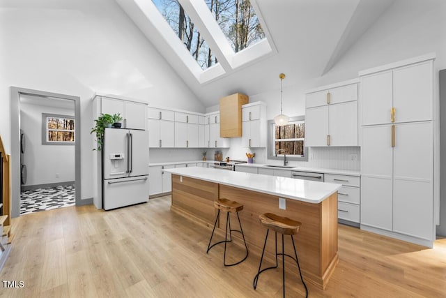 kitchen with tasteful backsplash, white cabinetry, hanging light fixtures, white refrigerator with ice dispenser, and high vaulted ceiling