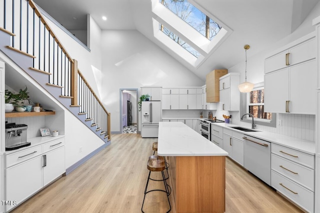 kitchen featuring white appliances, white cabinets, a kitchen island, sink, and hanging light fixtures