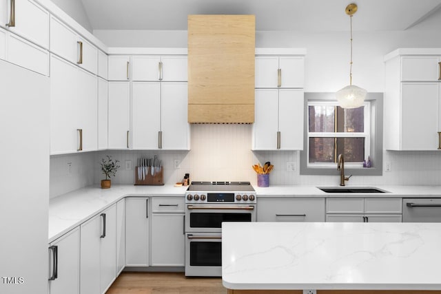 kitchen with double oven range, white cabinetry, sink, and decorative light fixtures