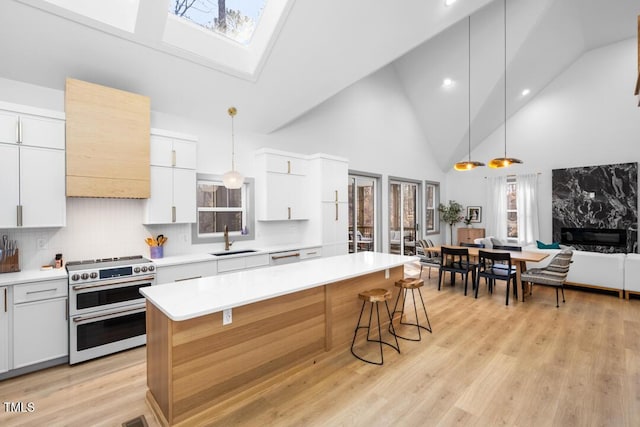 kitchen featuring a skylight, white cabinetry, tasteful backsplash, range with two ovens, and hanging light fixtures